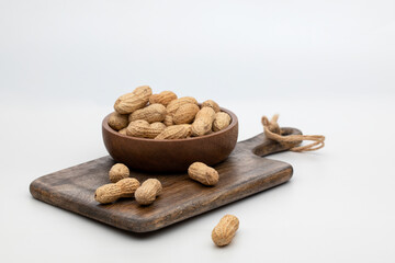 Unshelled peanuts in a wooden bowl on a white background
