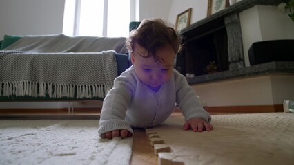 Baby lying on the floor, closely examining a wooden block, leaning down with curiosity, actively...