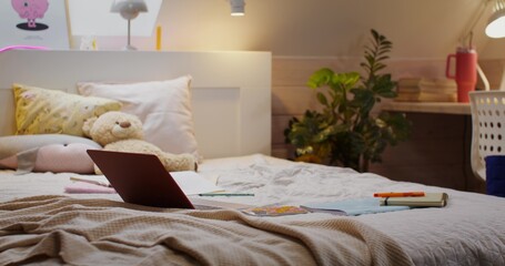 The bedroom of a young girl. An open laptop on the bed. There are no people