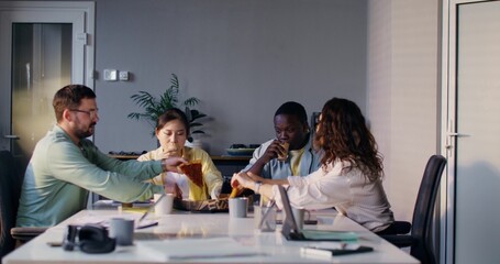 Colleagues eat pizza and talk during lunch in the office