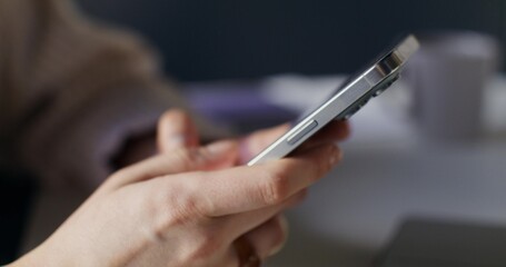 A woman uses a mobile phone while sitting indoors. Close-up of her hands, unrecognizable person