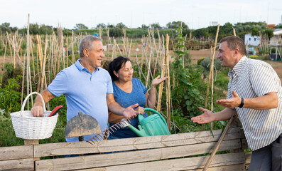 Couple of smiling elderly amateur gardeners discussing interesting topics with their male neighbor...