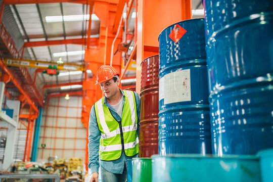 Engineers inspecting documents in heavy industrial warehouse surrounded by chemical barrels, ensuring safety protocols and operational accuracy in metalworking factory