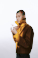 Naklejka premium Blurry woman wearing a brown jacket stands against a light background, creating a soft and mysterious atmosphere with muted colors and casual style.