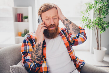 Tattooed man in bright checkered shirt talking on phone at home