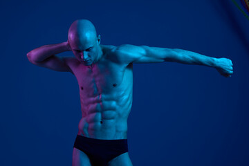 Athletic man posing in dramatic light, showcasing defined muscles. The image features a blend of blue tones, highlighting strength and vitality in a striking manner.