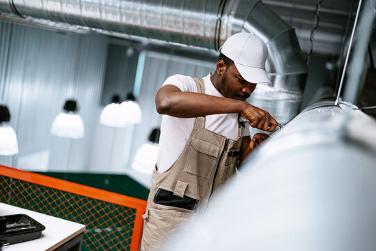 Worker performs maintenance on ventilation system in modern industrial space during daylight hours