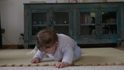 Baby touching mat with hands, focusing on textures and objects during independent playtime,...