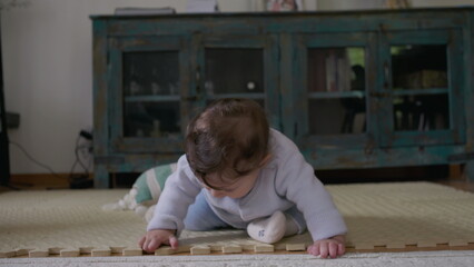Baby touching mat with hands, focusing on textures and objects during independent playtime,...