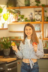Light-Skinned European Woman Smiling in Cozy Kitchen While Holding an Apple in Each Hand