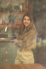 Fototapeta premium Light-Skinned European Woman Standing with Arms Crossed and Smiling in Cozy Kitchen