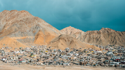 A scenic view of Leh town nestled in the rugged Himalayas, surrounded by dramatic brown mountains and traditional buildings, blending culture, architecture, and natural beauty in northern India