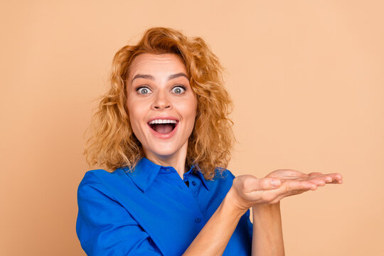 Fototapeta Smiling young woman in a blue shirt gesturing with enthusiasm against a beige background showcasing her joyful expression