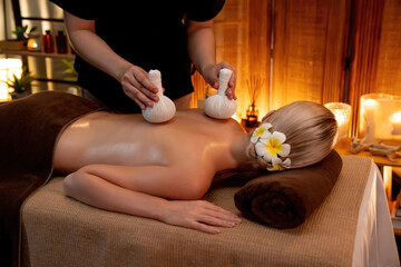 Hot herbal ball spa massage body treatment, masseur gently compresses herb bag on woman body....