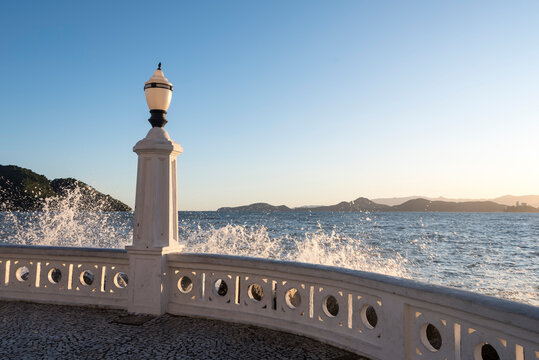 Santos city, Brazil. Old lamppost lit up. Waves hitting the traditional sea wall, a historic monument of the city. In the background, the bay of Santos.