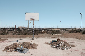 An abandoned basketball court, in a state of decay, with piles of rubbish and brushwood in the center of the field.