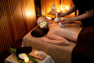 Hot herbal ball spa massage body treatment, masseur gently compresses herb bag on woman body....