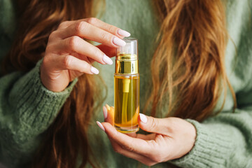 Fototapeta premium Woman holding cosmetic oil. Natural serum in hands. Organic skincare product in bottle. Beauty treatment concept. Moisturizing care routine. Selfcare and wellness. Female hands with nude manicure.