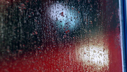 Condensation and raindrops forming textured patterns on glass with red and blue hues in the background, abstract water droplets creating a unique interplay of light and color