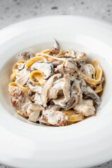 A plate of creamy pasta with mushrooms and chicken, served in a white bowl. dish features fettuccine noodles coated in a rich, white sauce with visible pieces of saut&eacute;ed mushrooms and grilled chicken