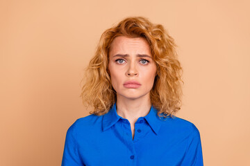 Beautiful young woman with red hair wearing blue shirt against beige background expressing a...