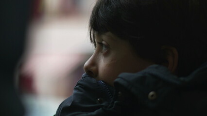 Close-up side profile of young boy resting his chin on jacket, gazing into distance with thoughtful...