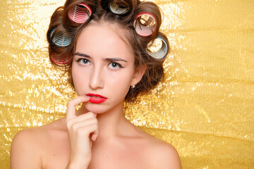 Beautiful girl in hair curlers isolated on gold
