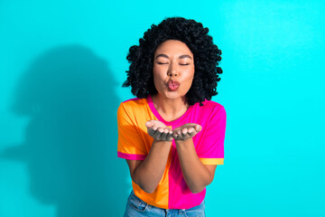 Young woman blowing a kiss gesture wearing colorful casual outfit against a bright turquoise...