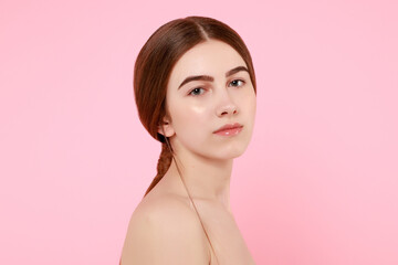 Beautiful young girl touching her perfect skin on pink background.