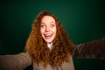 Young businesswoman with curly red hair expressing excitement against a solid green background