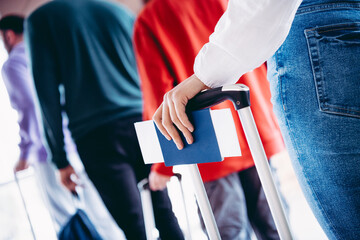 Young woman with passport and suitcase standing in line for check-in at airport, preparing for a...