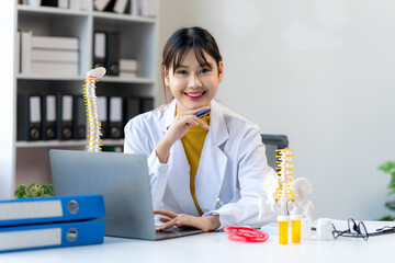 Smiling Asian Doctor at Desk with Spine Model