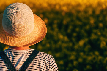 Female farm worker looking over blooming canola rapeseed field in spring sunset