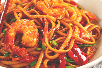 udon stir-fry shrimp noodles with red bell pepper and green onion, served in a black bowl, with chopsticks, gray background,
