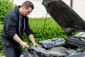 The car broke down while traveling. A frustrated man near a broken car with an open hood far outside the city.  A young guy looks under the hood of a car.