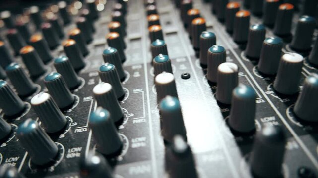 Pro audio mixing board faders and knobs. Quick slider shot across multi-track music recording equipment.