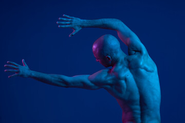 Dynamic man posing with expressive gestures against a dark blue background, showcasing athletic physique and emotional energy. The image captures movement and passion.