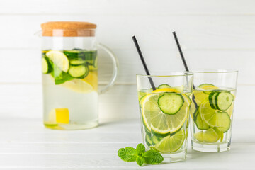 Cucumber water with lemon, lime and mint on a wooden table. Water infused with sliced ​​cucumber in a drinking glass. Tonic refreshing drink. Cucumber lemonade.Summer natural cooling drink.Copy space