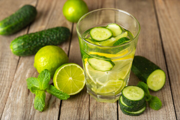 Cucumber water with lemon, lime and mint on a wooden table. Water infused with sliced ​​cucumber in a drinking glass. Tonic refreshing drink. Cucumber lemonade.Summer natural cooling drink.Copy space