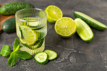 Cucumber water with lemon, lime and mint on a wooden table. Water infused with sliced ​​cucumber in a drinking glass. Tonic refreshing drink. Cucumber lemonade.Summer natural cooling drink.Copy space