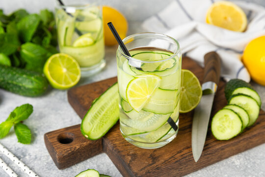 Cucumber water with lemon, lime and mint on a wooden table. Water infused with sliced ​​cucumber in a drinking glass. Tonic refreshing drink. Cucumber lemonade.Summer natural cooling drink.Copy space
