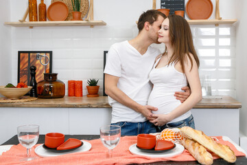 Young married couple embraces standing near table in kitchen.