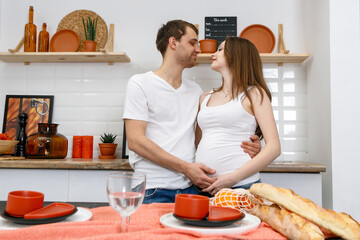Young married couple embraces standing near table in kitchen.