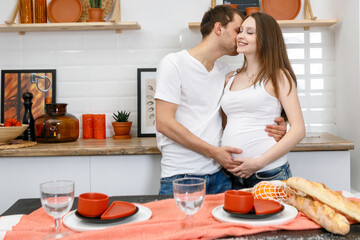 Young married couple embraces standing near table in kitchen.