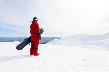 Snowboarder stands on backcountry slope and holds snowboard.