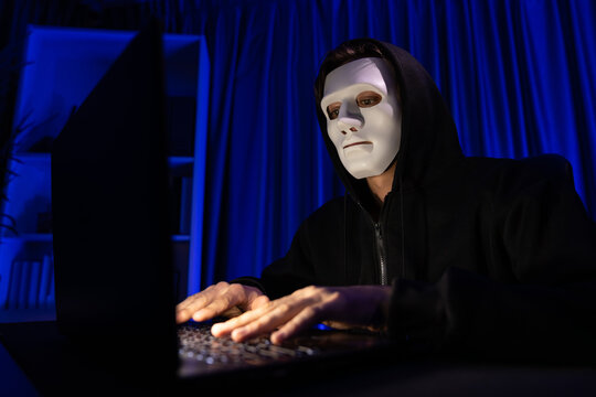 White criminal anonymous mask installing coding password encryption by programming hack, trying to make insecure thorough privacy taking massive database on computer for ransom to company. Pecuniary.