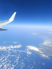 Fototapeta premium Coastal aerial view from airplane window flying above deep blue sea