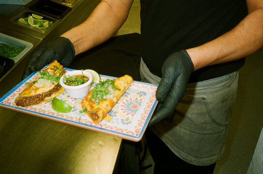 Midsection of man holding tray of freshly prepared tacos in kitchen