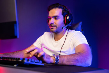 Serious face gaming streamer concentrating gaming players trying to pass at mission completed, using headset and mic for communicate others on streaming live at neon lighting studio room. Surmise.