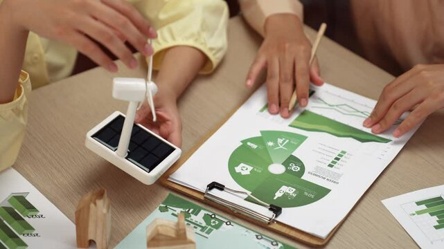 Business team analyze green power graph usage. Coworker with windmill model represented using clean energy and wooden block symbolized eco house choosing way to decrease carbon in future. Delineation.